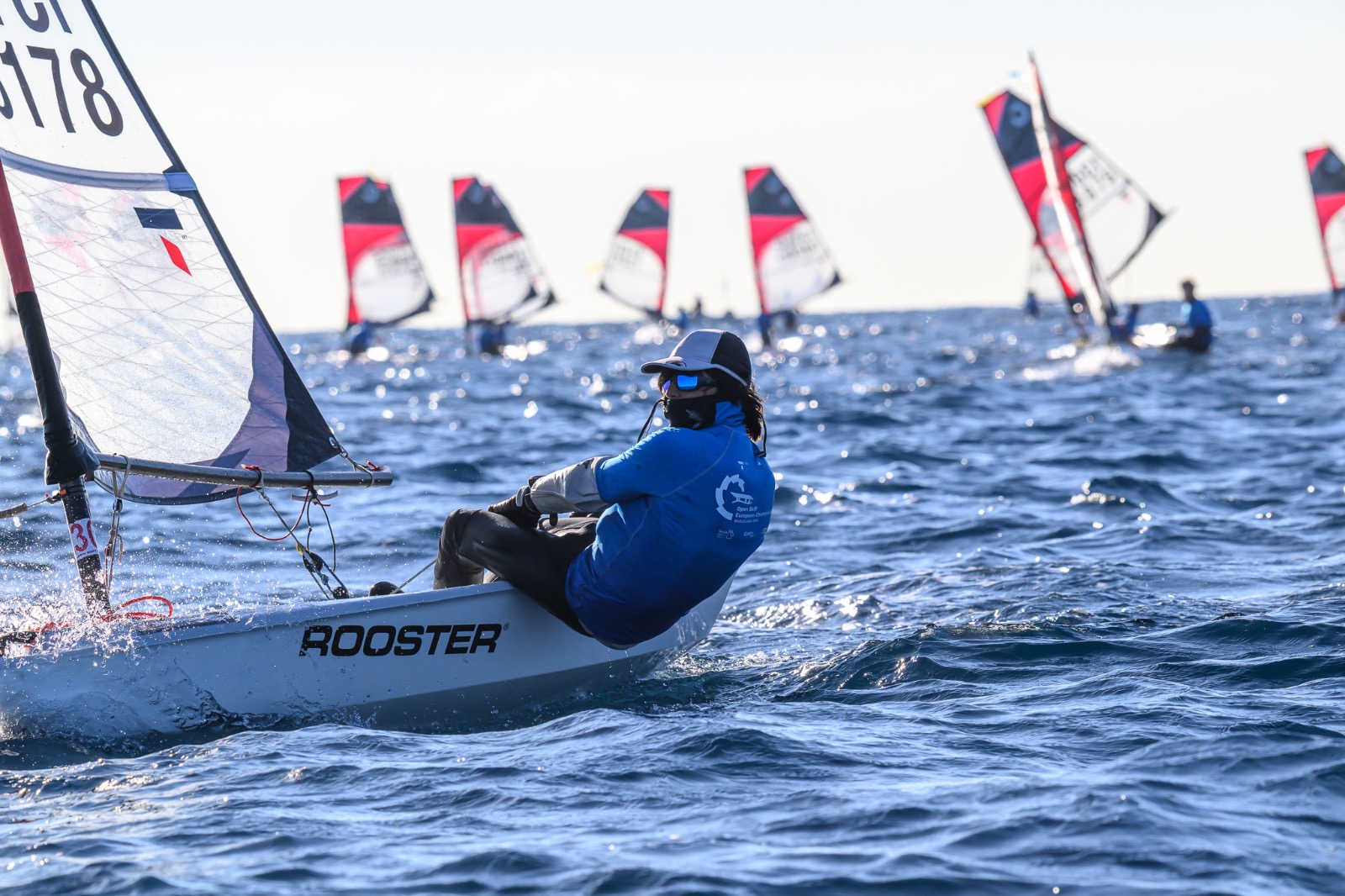 Dinghy sailor hiking out hard while planing through blue water